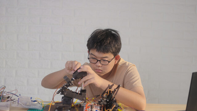 Asian young student assembling a robotic arm at home with electronics and robotics equipment. Concept of STEM education, engineering skills, innovation, and hands-on technology learning.