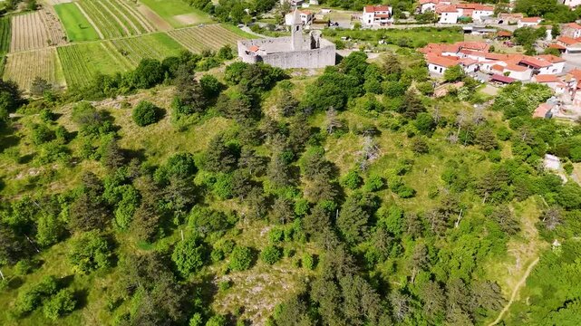 Drone view of the stone fortified church of Holy Trinity in Hrastovlje, Slovenia, overlooking vineyards, rural roads, and green countryside.