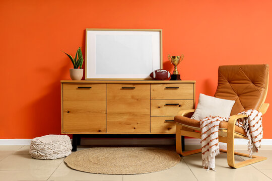 Modern living room interior with wooden sideboard, blank frame, leather armchair, and orange wall decor