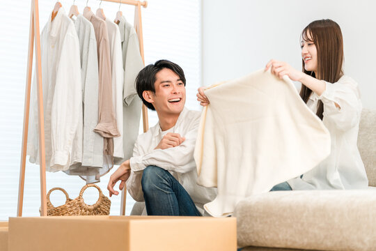 A young Asian couple, married, tidying up their clothes and changing their wardrobe in their living room.