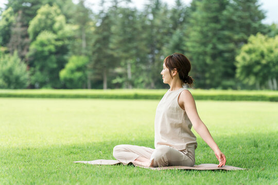 Asian women taking deep breaths, stretching, and doing yoga in a park.