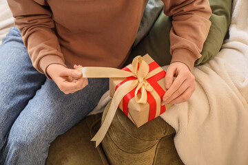 Fototapeta premium Person tying golden ribbon on brown gift box with red ribbon, holiday celebration and special occasion present, this activity represents the joy of holiday celebrations and special occasions