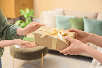 Fototapeta premium Hands exchanging gift box wrapped in brown paper with gold ribbon, present giving and receiving