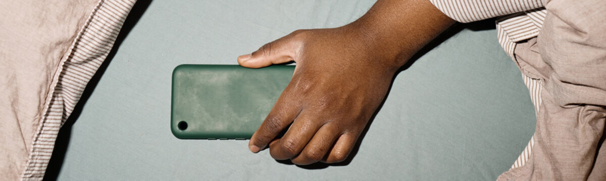 Close up of hand holding smartphone in bed, showing compulsive screen use at home and digital fatigue. Ideal for content about tech addiction, sleep disruption