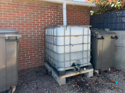 Rainwater harvesting tank beside brick wall and trash bins