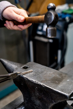 Blacksmith shaping hot metal on an anvil with hammer in a traditional workshop.