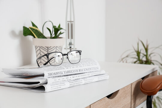 Reading glasses on stack of newspapers with houseplant on modern white desk business information and news update, this setup business information news updates and the daily routine of staying informed