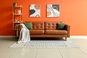 Modern living room interior design with orange wall, brown leather sofa, and abstract art decor © Pixel-Shot
