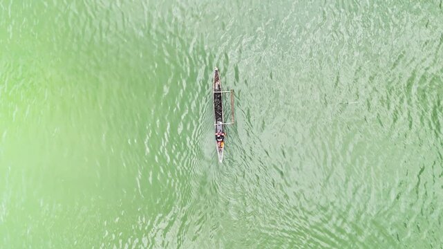 Aerial drone view of a lone fisherman paddles a dugout canoe through the vibrant green waters of Inner Malampaya Sound in Philippines