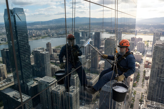 Window washers cleaning skyscraper facade high above city