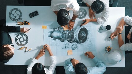 Top view of engineer team writing idea on sticky notes at meeting while discussing about turbine engine or electric generator at meeting table with metal gear, calculator and equipment. Alimentation. © InfiniteFlow