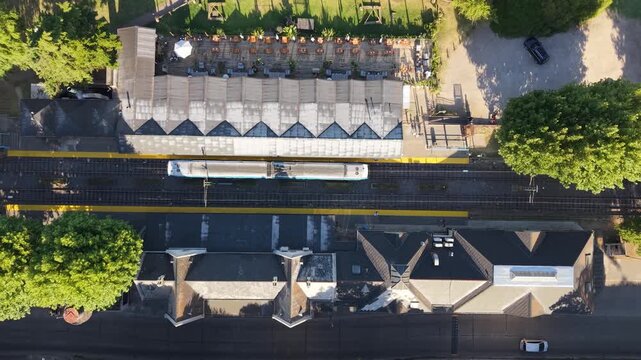 Vista a&eacute;rea cenital de tren partiendo desde estaci&oacute;n ferroviaria en un d&iacute;a soleado con infraestructura de transporte urbano