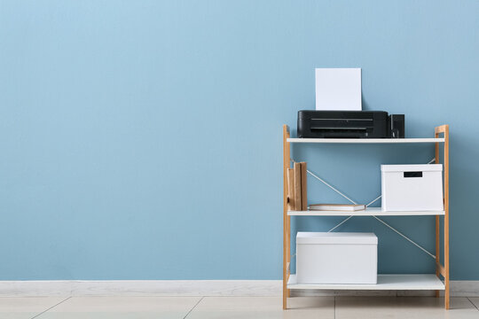 Home office printer and storage shelf with books and boxes against a blue wall background, the shelf is positioned against a light blue wall, creating a clean and organized workspace