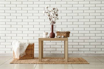 Modern home interior decor with cotton branches in vase, woven baskets, and white brick wall background © Pixel-Shot