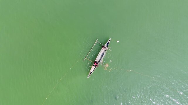 Aerial drone view of a lone fisherman paddles a dugout canoe through the vibrant green waters of Inner Malampaya Sound in Philippines