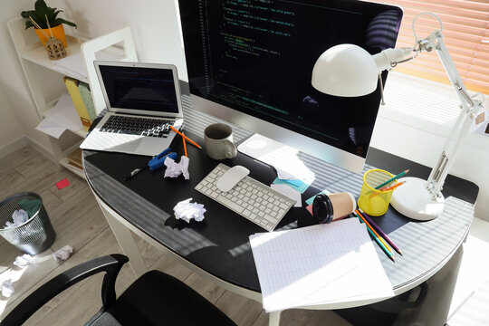Messy home office desk with computer code, laptop, and crumpled paper, remote work environment