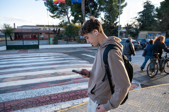 Teenage student checking smartphone while walking to school near a pedestrian crossing