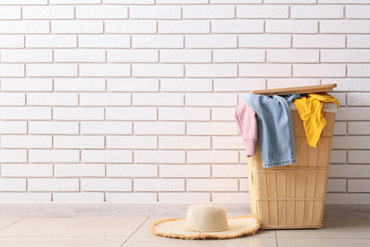 Laundry basket with clothes and straw hat against white brick wall background, home chores and domestic life