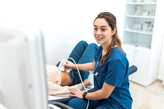 Professional female doctor in blue scrubs performing abdominal ultrasound scan on patient in clinic examination room. Healthcare concept with medical worker using sonogram machine for diagnosis.