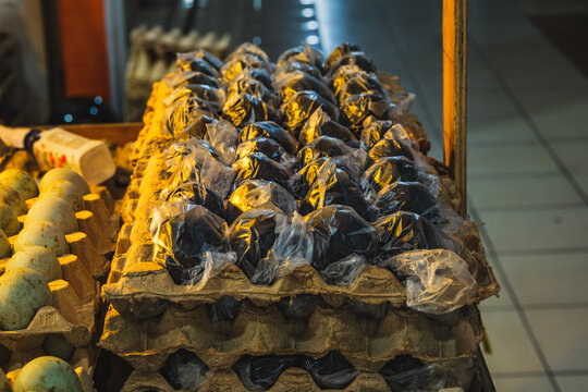 Black century eggs wrapped in plastic on trays at market