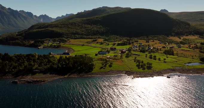 Aerial view of Kvitnes Gaard farm and restaurant from over the fjord with sun reflecting on the water in Northern Norway