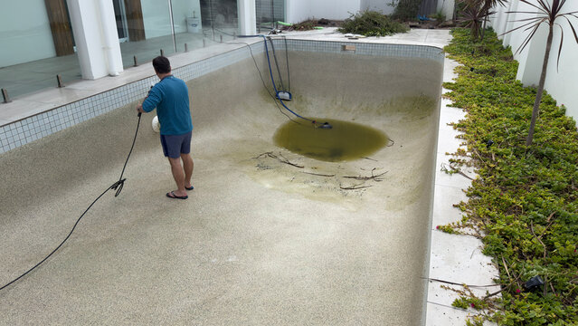 Man Cleaning Empty Swimming Pool with High Pressure Water Washer