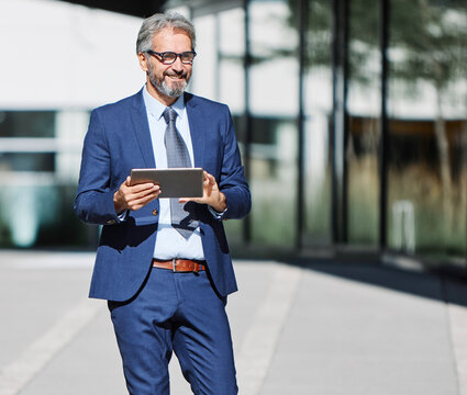 Portrait of a happy smart inteligent senior businessman smiling using a tablet computer standing in the front of the office building