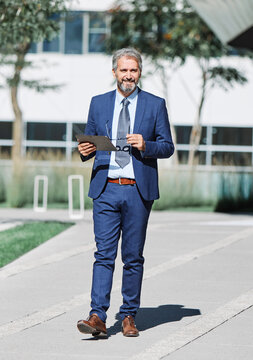 Portrait of a happy smart inteligent senior businessman smiling using a tablet computer standing in the front of the office building