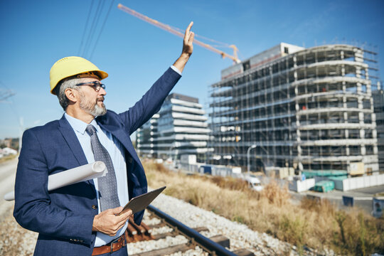 senior businessman architect wearing a protective helmet using a tablet and a blueprint on the construction site