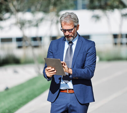 Portrait of a happy smart inteligent senior businessman smiling using a tablet computer standing in the front of the office building