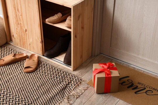 Home entryway with wooden shoe cabinet, welcome mat, and gift box, organized modern interior design