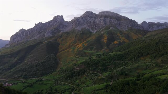 Picos de Europa, Spain - Aerial drone footage of epic mountain range in northern Spain at dusk with slow tilt up from the forested landscape to the rocky massif