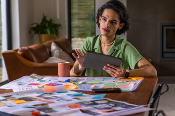 Obraz premium Asian man sitting at wooden table in living room, holding tablet folio reviewing sticky notes