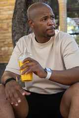 Fototapeta premium Adult African man sitting on bench by brick wall holding plastic cup with straw looking right