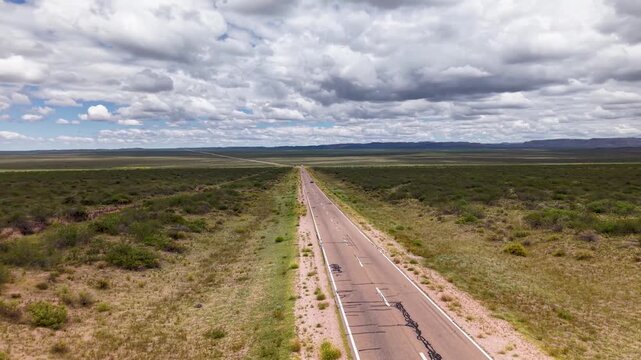 Ruta atravesando paisaje &aacute;rido con vegetaci&oacute;n nativa, autos circulando y nubes en un d&iacute;a soleado