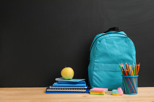 Back to school education with blue backpack, stack of notebooks, apple, and pencils on wooden desk