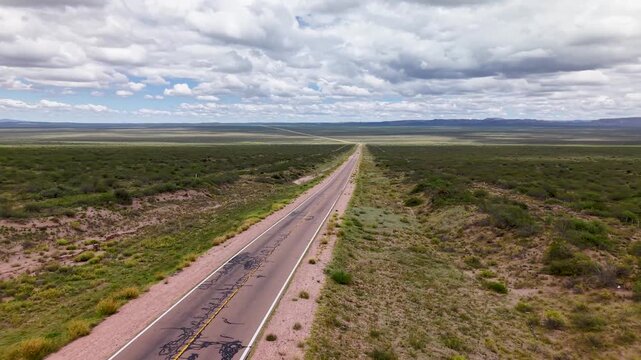 Ruta atravesando paisaje &aacute;rido con vegetaci&oacute;n nativa, autos circulando y nubes en un d&iacute;a soleado