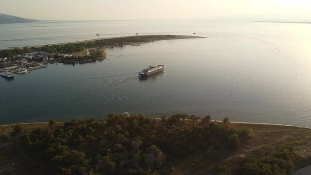 Drone aerial view of a ferry boat sailing near a coastal harbor town at sunset