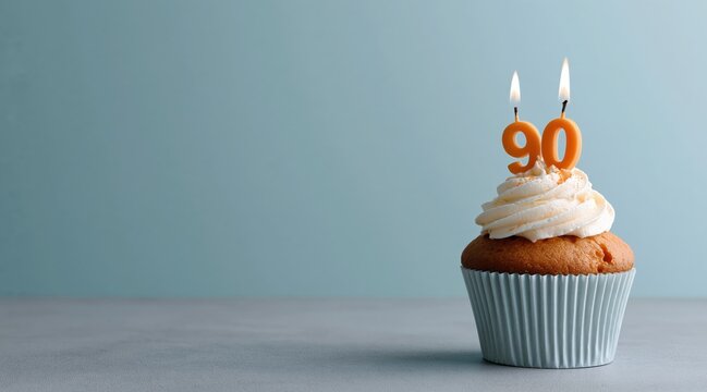 Cupcake with lit number ninety candles on blue background with copy space
