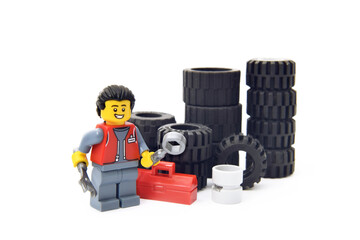 Obraz premium Editorial illustrative image of lego minifugure of mechanic with tires in car service of repair isolated on white. Popular children toy of plastic bricks constructor.