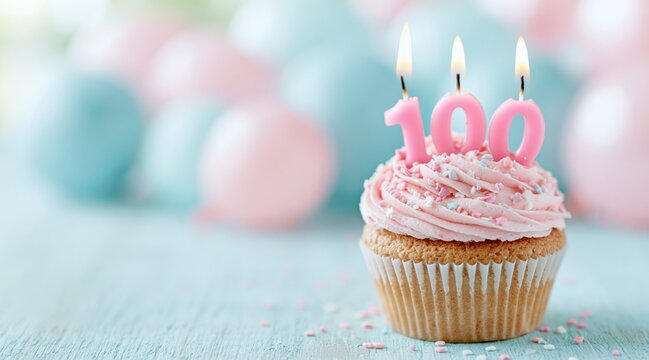 Birthday cupcake with pink frosting and number 100 candles against blurred balloons
