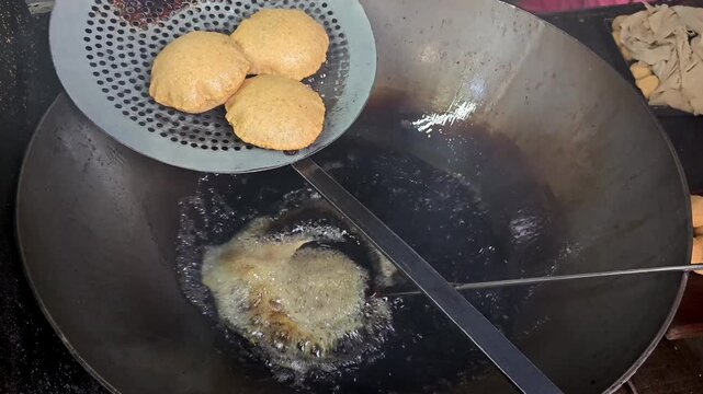 Indian street food vendor deep frying fresh puris in a large wok with boiling hot oil