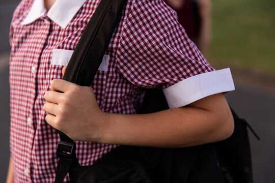 close up of a gingham maroon school dress work by a school girl with a backpack
