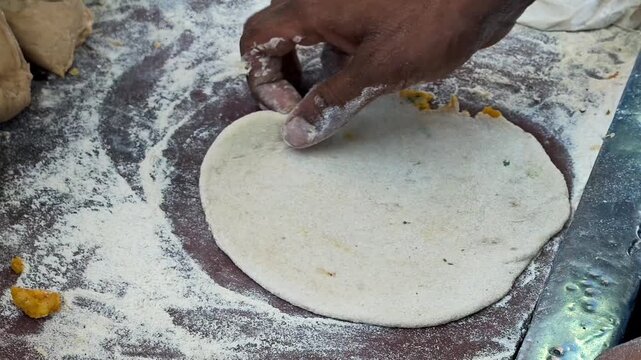 Indian street food vendor rolling and shaping aloo paratha by hand