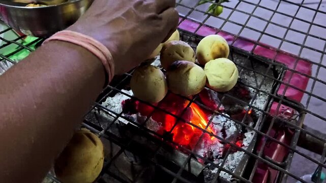 Traditional Indian Litti Chokha or Baati being roasted on a hot charcoal grill over burning embers