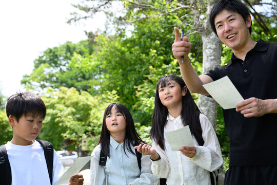 新緑の自然の中で先生と一緒に地図を見て発見に驚く小学生たち