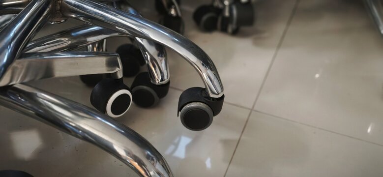 Close-up of office chair wheels and chrome metal base on office floor.