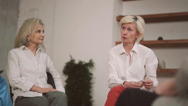 Aged woman talking about divorce or psychological trauma in group therapy. Mutual support group for people in difficult life situation or oncological patients, psychological help and supporting