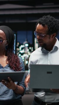 Vertical video showing portrait of engineering team developing AI algorithms in high rise office. Teamworking colleagues debug 3D neural network brain models shown on screen.
