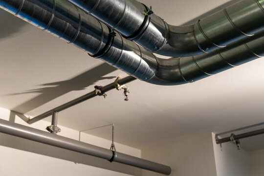 Exposed metal HVAC ventilation ducts and sprinkler pipes on a white ceiling. Modern industrial architecture.